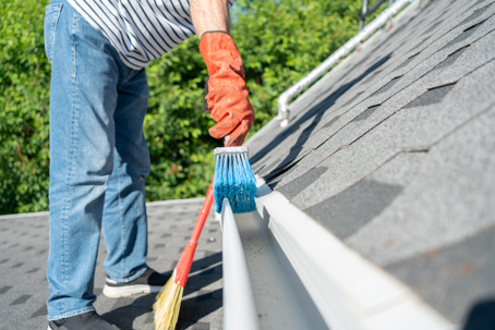 a person cleans white gutters on a shingled roof
